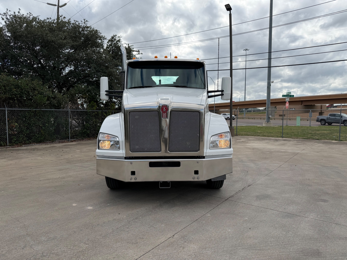Kenworth T880 conventional daycab front view showing large grille, bumper, and headlights in a parking lot.