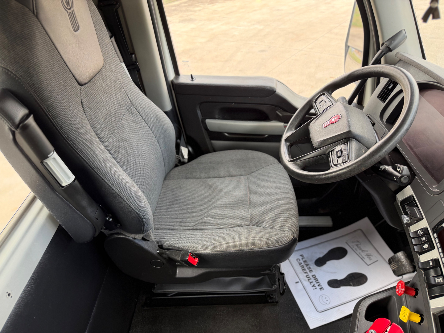 Kenworth T880 interior driver seat and steering wheel view showing grey fabric seats and dashboard. 