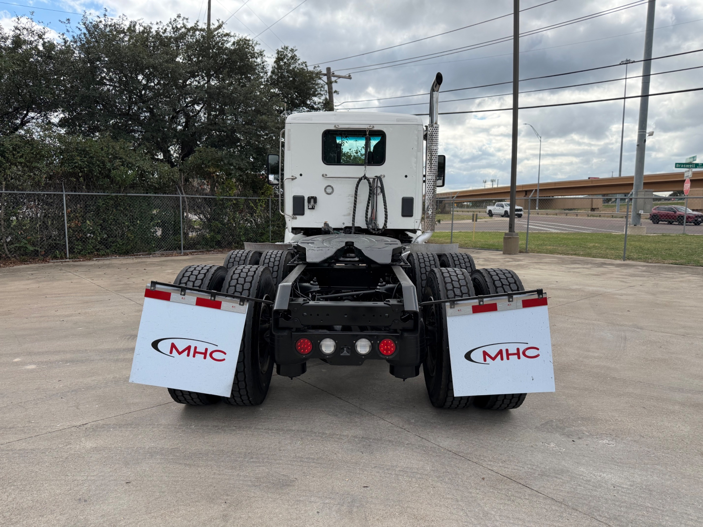 Kenworth T880 rear view showing dual rear axles and white mud flaps with MHC logos.