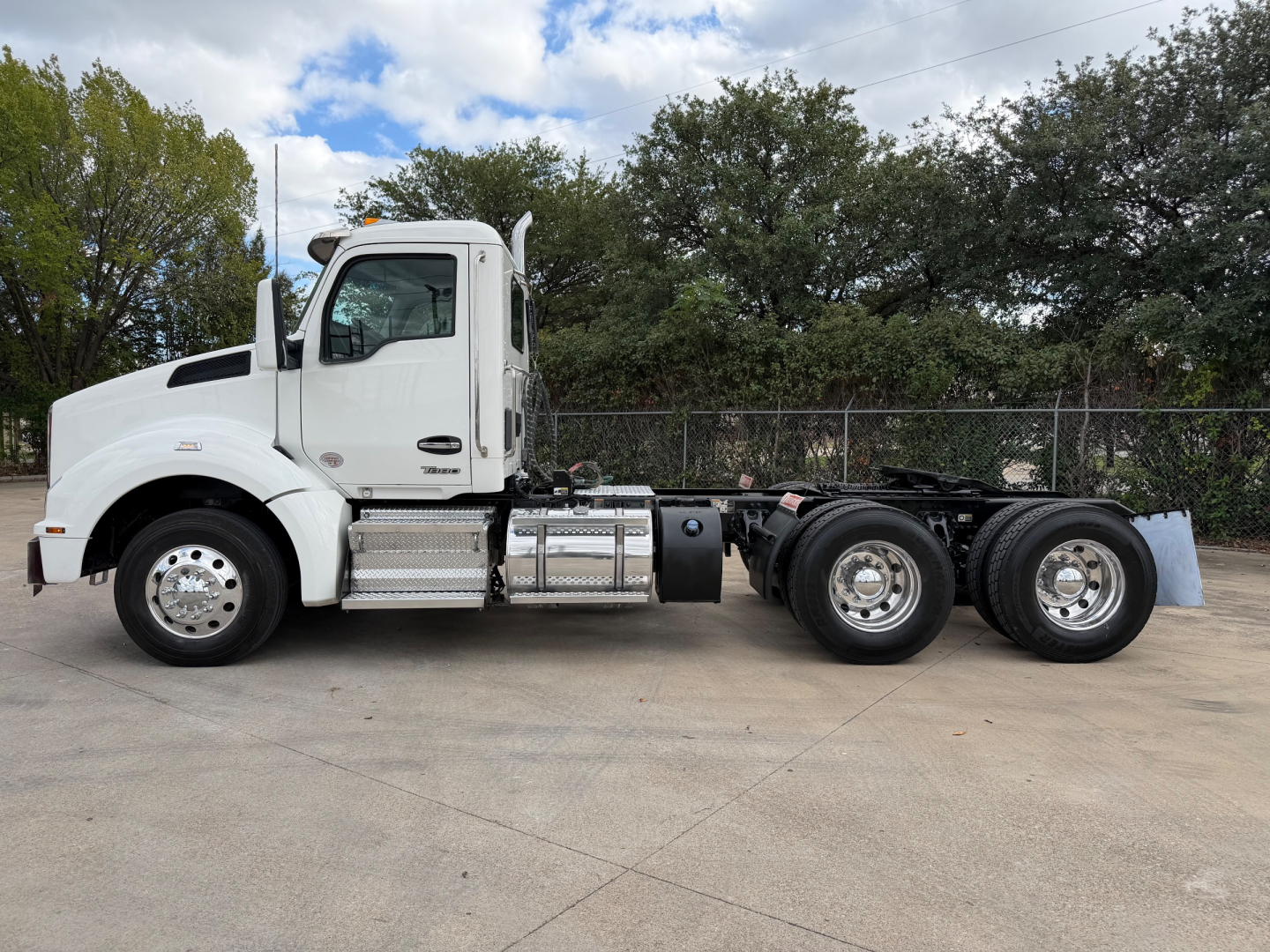 Kenworth T880 tractor unit side view showing white cab and dual rear axles with chrome fuel tanks and steps.