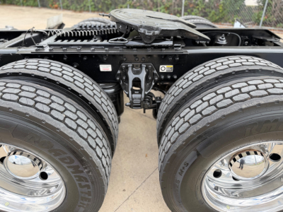 Kenworth T880 rear axle assembly showing dual rear wheels and tires with chrome hubcaps and suspension components visible.