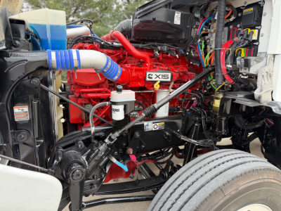 Kenworth T880 engine bay showing Cummins X15 badge and red engine with blue silicone hose, black chassis and wiring harnesses.