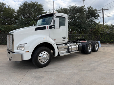 White Kenworth T880 conventional daycab truck with dual rear axles, side fuel tanks, chrome steps, and large grille.