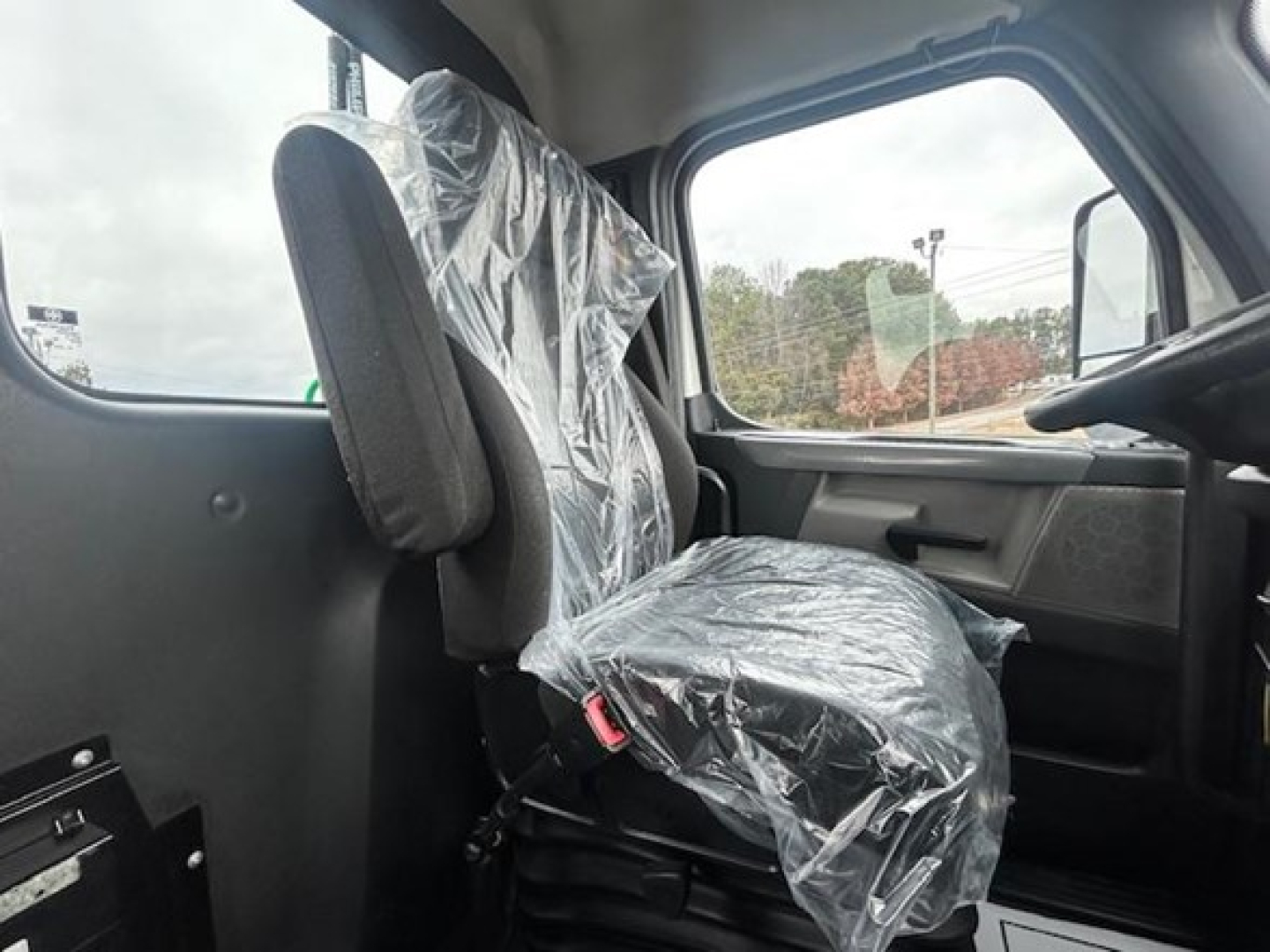 Truck cab interior with plastic seat coverings, driver seat and passenger side visible, window view outside.