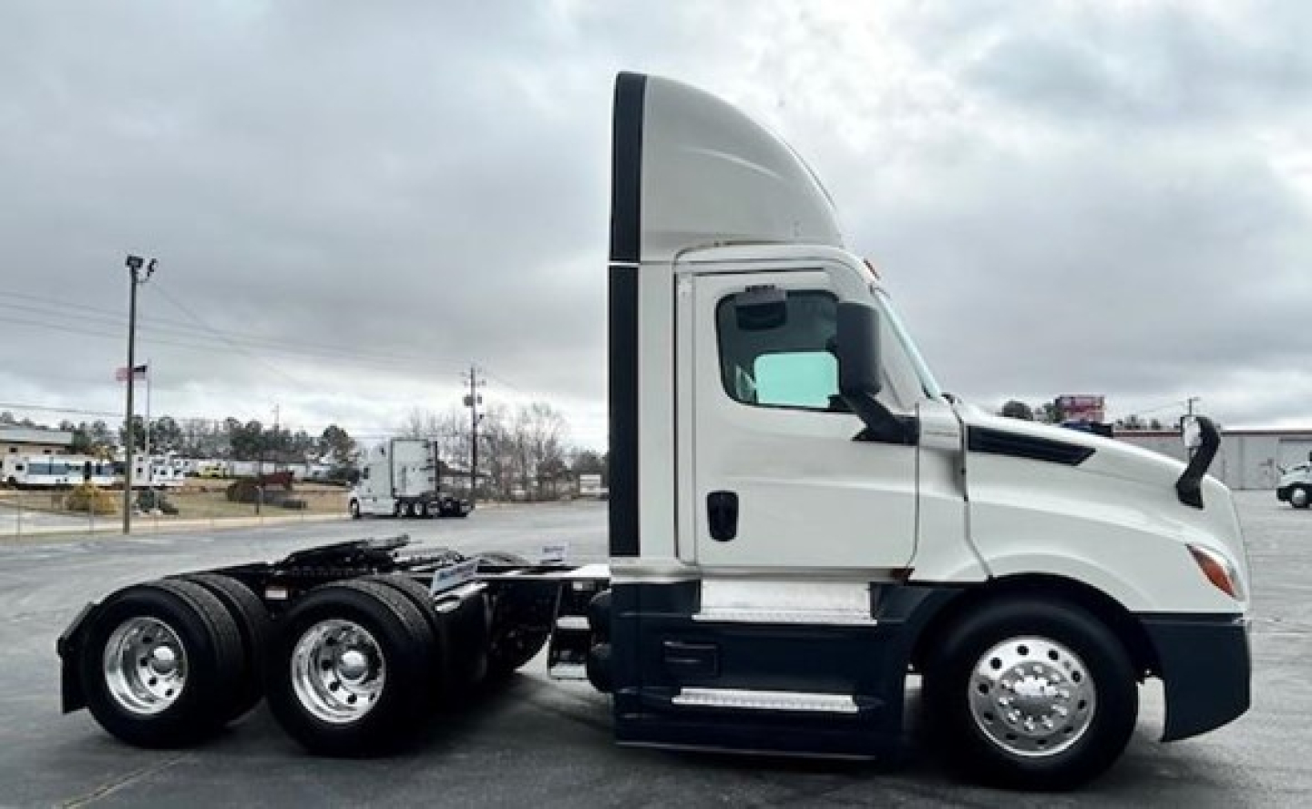 Truck side view of a 2022 Freightliner Cascadia 126 Day Cab showing front wheel area and cab with sleeper in white and black accents.