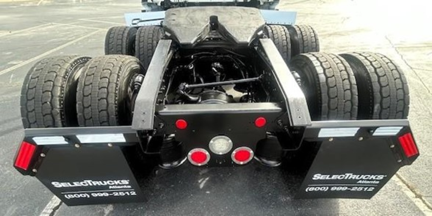 Tractor-trailer rear view showing chassis and fifth-wheel area with dual rear axles and mud flaps; red reflectors and taillights visible.