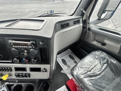 Dashboard and passenger seat area of a 2022 Freightliner Cascadia 126 day cab truck cab interior. Visible text includes 'FREIGHTLINER' on the dash, various control dials, radio, and climate controls. Shows front passenger seat covered in pl
