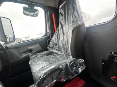 Truck cab interior seat covered in plastic with driver door and window visible; Freightliner Cascadia 126 cab in view.
