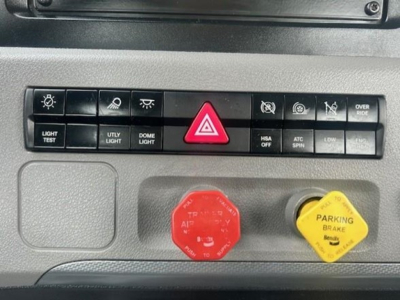Dash panel with hazard light triangle button, various control buttons, red emergency stop knob, and yellow parking brake knob on a Freightliner Cascadia dash.
