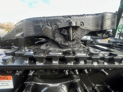 Engine bay view of a Freightliner Cascadia showing a metal lift mechanism and black painted components with bolts and hydraulic lines.