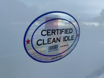 Sticker on Freightliner Cascadia showing 'CERTIFIED CLEAN IDLE' with holographic seal on blue vehicle surface