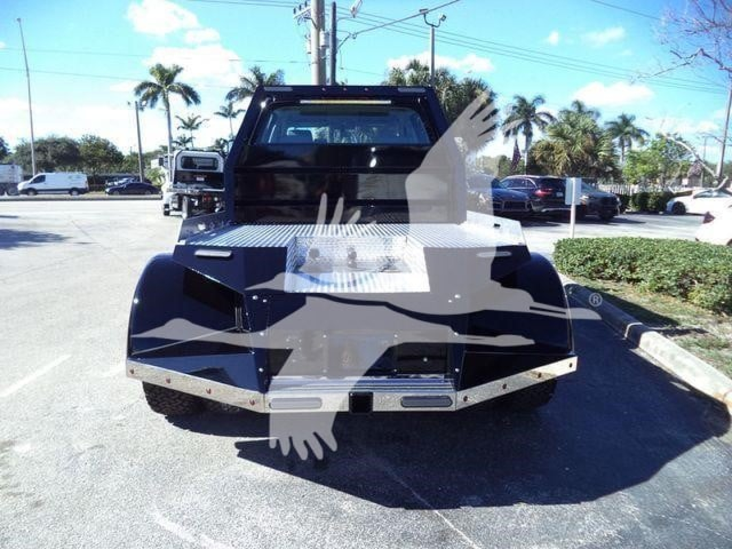 Truck bed of a 2023 International CV tow truck with flatbed, showing a diamond plate toolbox and black body panels. The rear of the cab is visible with a slim rear window and light bar above.