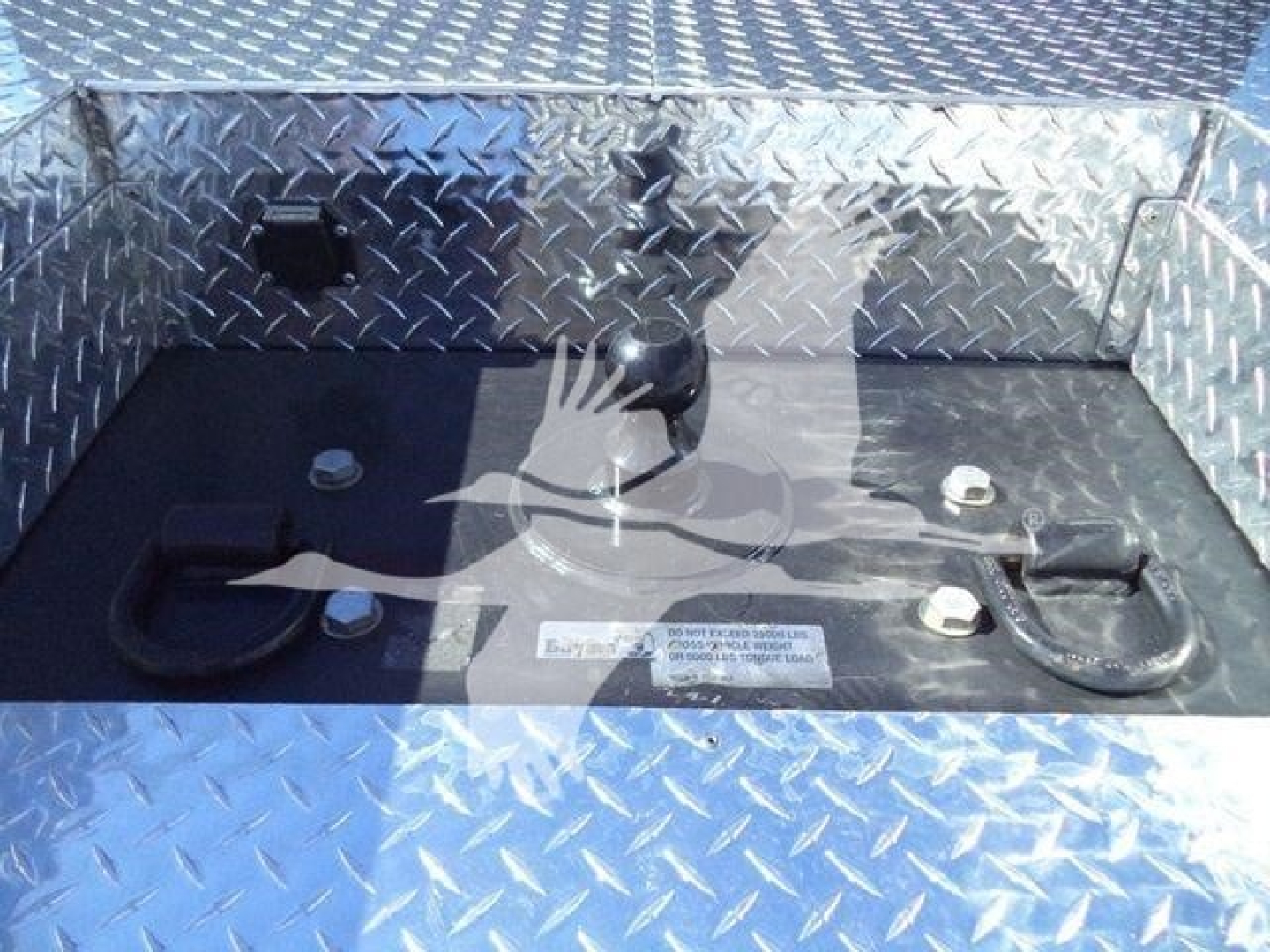 Truck bed with tie-down anchors and a shifter in a diamond plate aluminum bed; label plate visible on black surface.