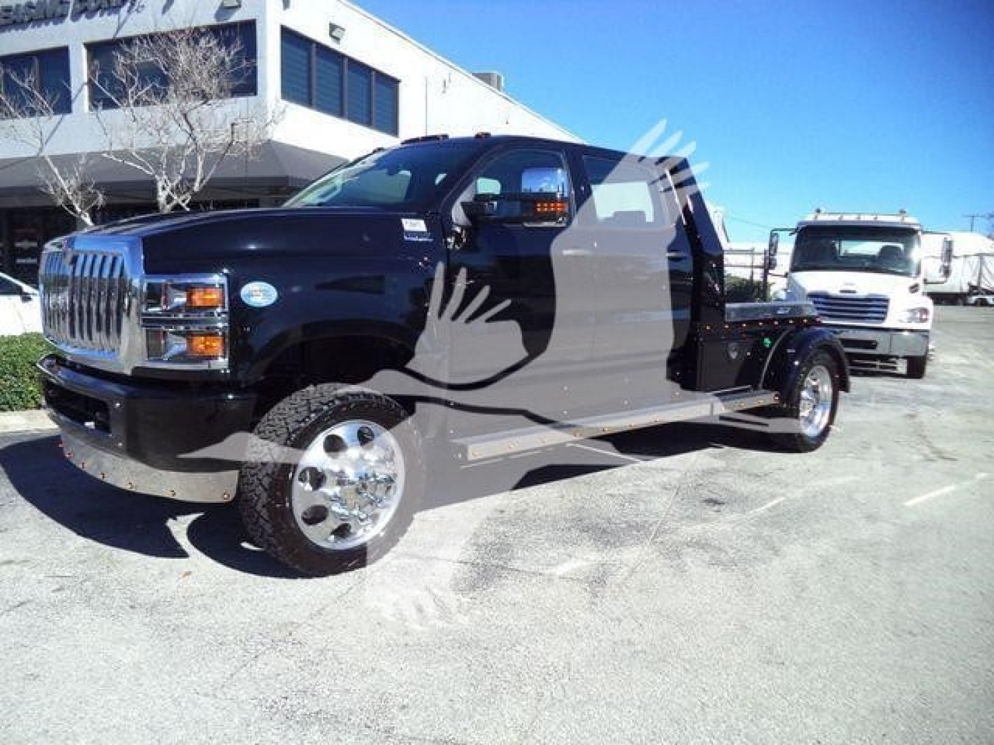 2023 International CV truck in a dealership lot, black cab with chrome wheels and extended cab, flatbed chassis visible.