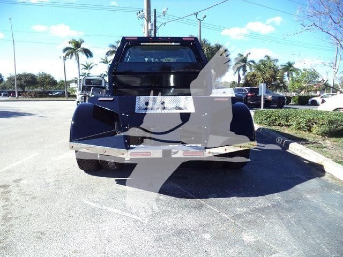 Front view of a blue International CV tow truck with a lift or bed, visible parking lot and palm trees in background.