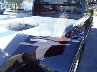 Flatbed tow truck with diamond plate deck and side rails, black cab, and chrome wheel rims visible.