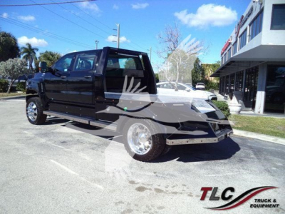 Truck in dealership lot showing a black 2023 International CV Toter with open cabin and flatbed, chrome wheels, and dealership building in background.