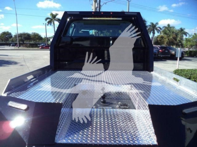 Truck bed with diamond plate aluminum flatbed and rear cab window visible; metallic surface reflects sunlight.