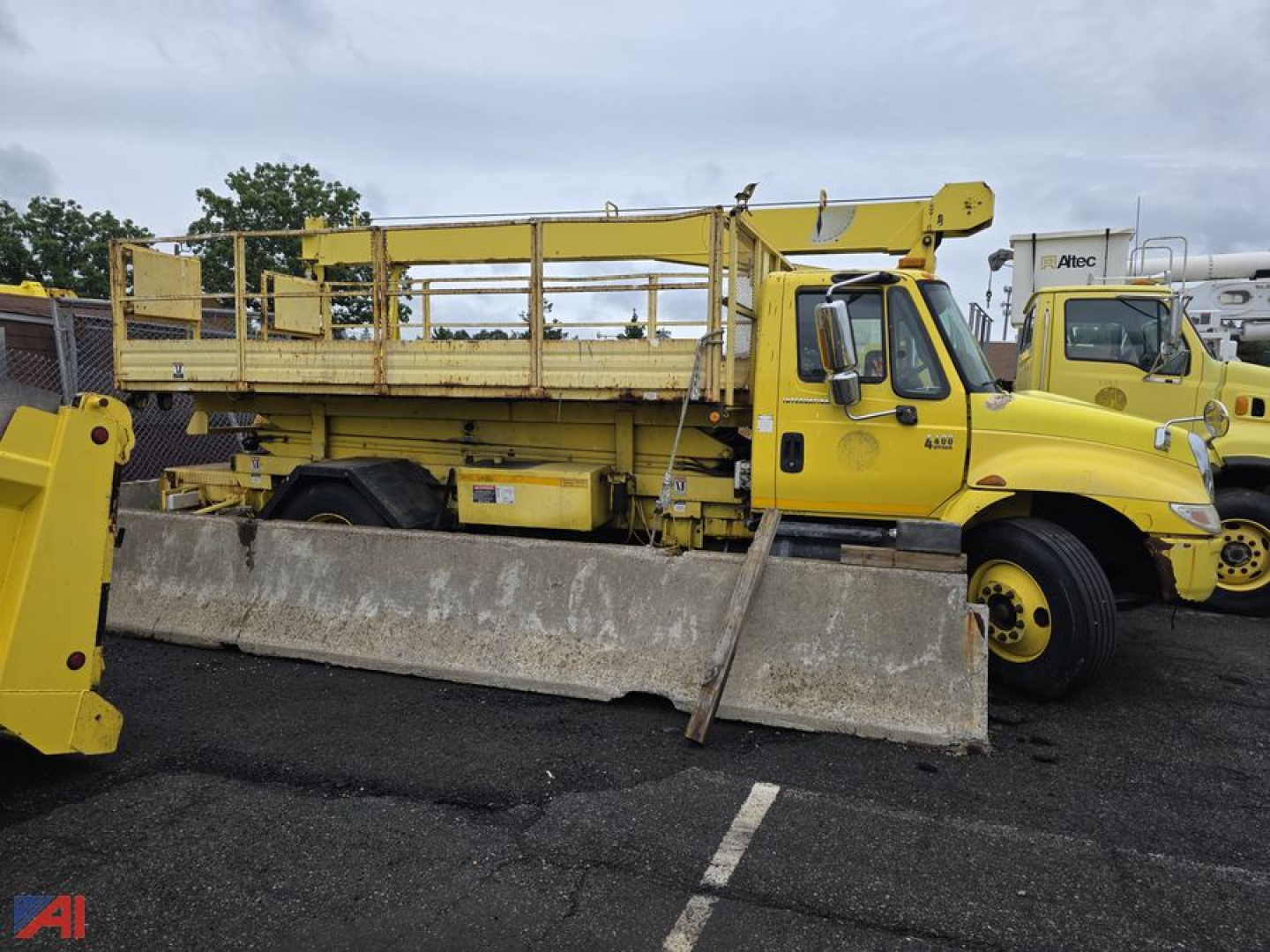 Truck chassis with Altec aerial unit and large concrete paver blade attached, 2004 International DuraStar 4400 stake truck in yellow showing utility equipment and crane components attached