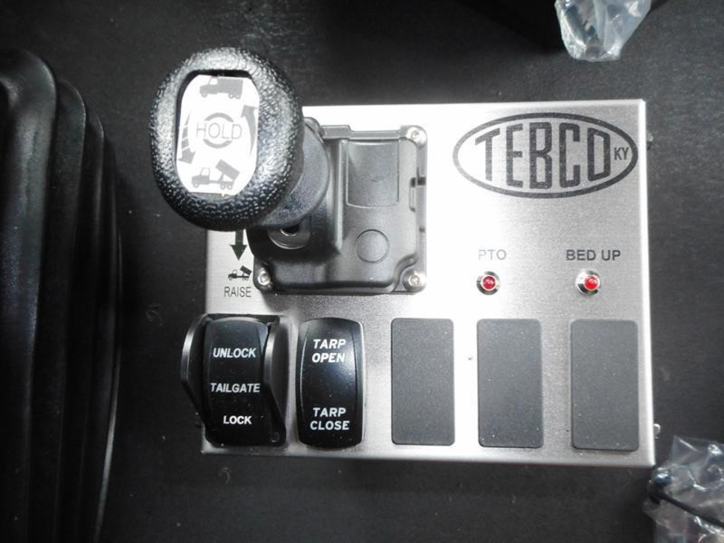 Panel with TEREX badge and controls including PTO, bed up indicators, and lever knob on a dump truck cab