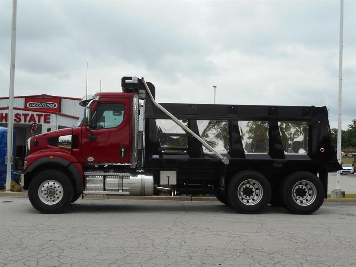 Western Star 47X dump truck side view showing red cab and black dump body with chrome fuel tanks and dual rear axles.