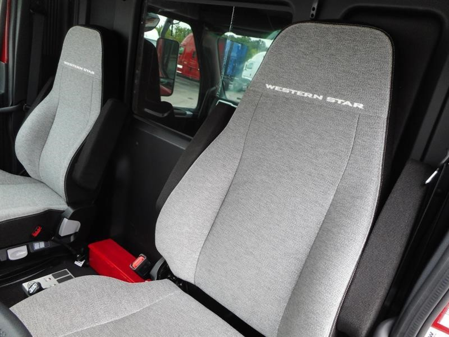 Western Star 47X truck interior seats with 'WESTERN STAR' embroidery on light gray fabric. Front seats visible with gray upholstery, red toolbox on floor, control panels near middle console.