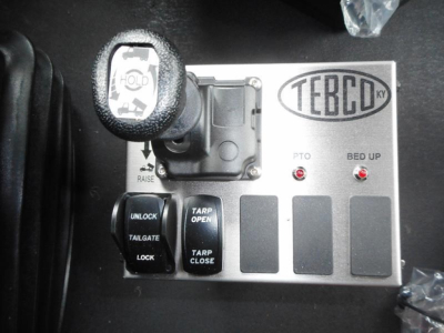 Panel with TEREX badge and controls including PTO, bed up indicators, and lever knob on a dump truck cab