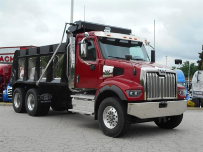 Western Star dump truck in red cab with black dump body, chrome grille and heavy-duty chassis, side mirrors, and steps visible.