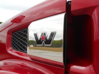 Western Star emblem on a red truck hood with chrome grille and side mirror reflecting the surroundings