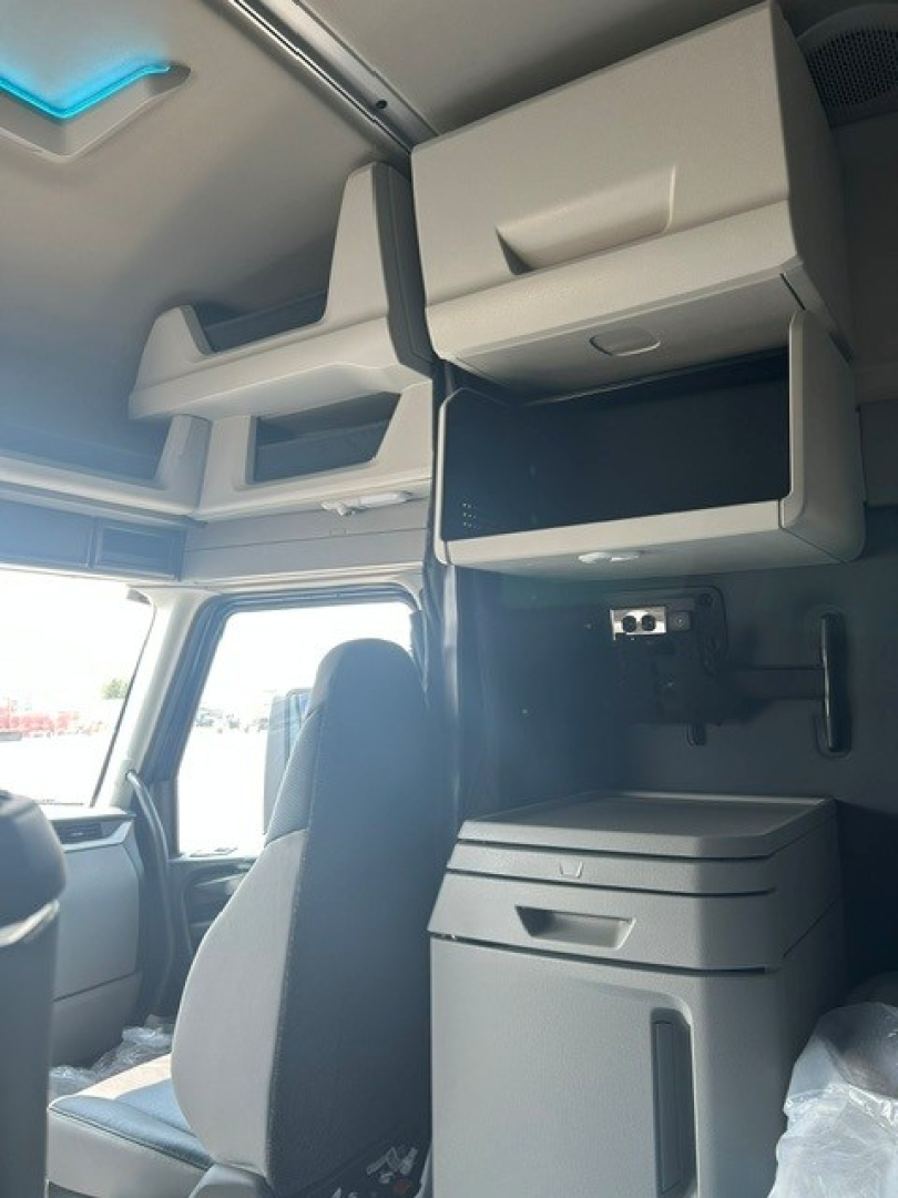 Cab interior of a Volvo VNL truck showing overhead storage shelves, a mounted drawer unit, and a small cabinet with a shelf in the sleeper area.