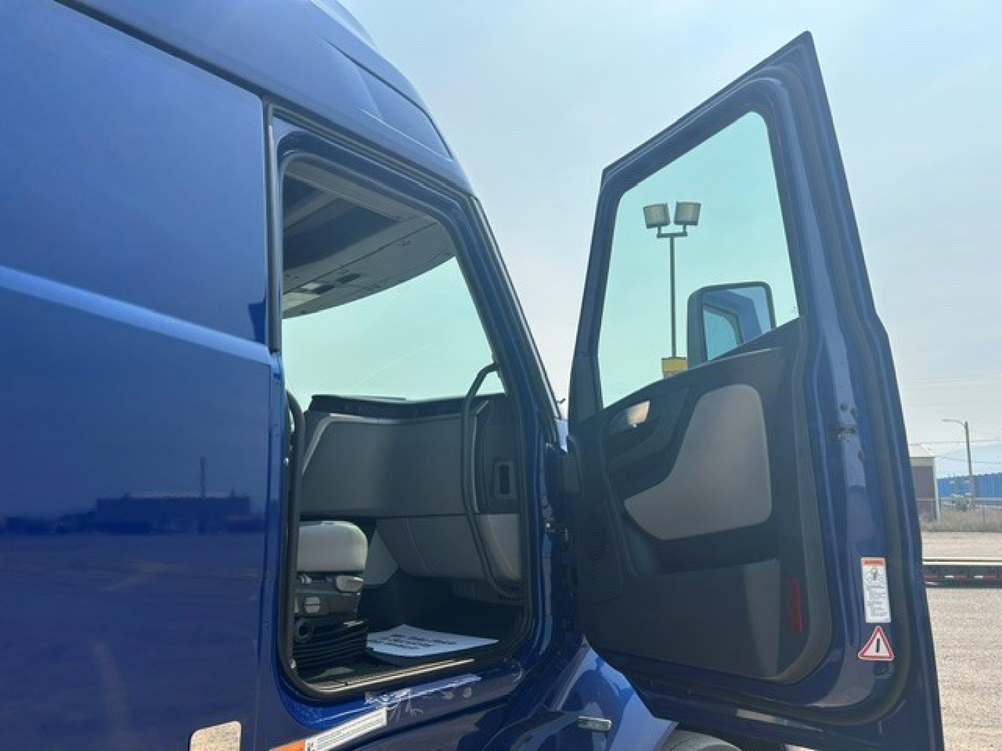 Volvo VNL truck cab door open showing blue exterior and interior seating with door panel and window.