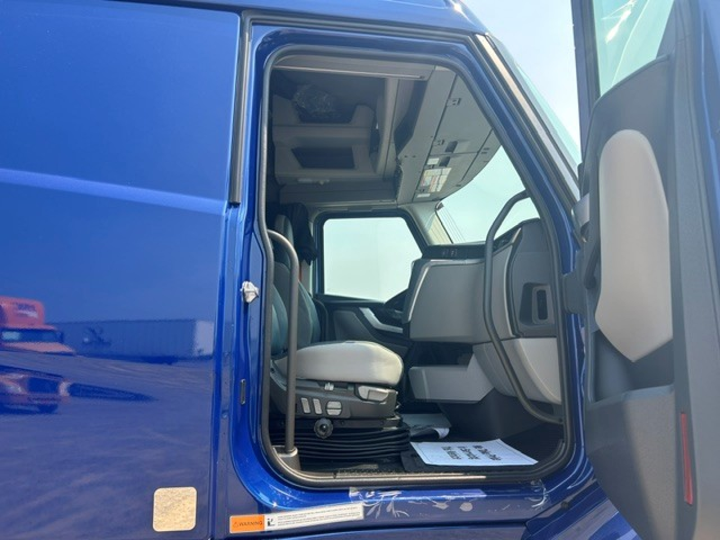 Cab interior of a blue Volvo VNL64T840 truck cab showing driver seat and dashboard from the doorway.