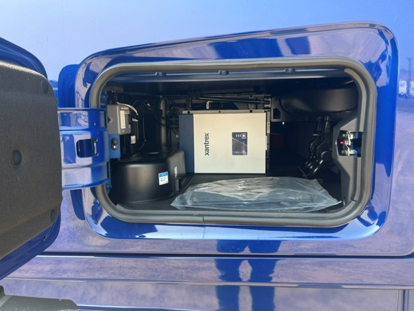 Compartment of a blue Volvo VNL truck showing a white Generac?/exchange unit inside a storage bay with a plastic cover.