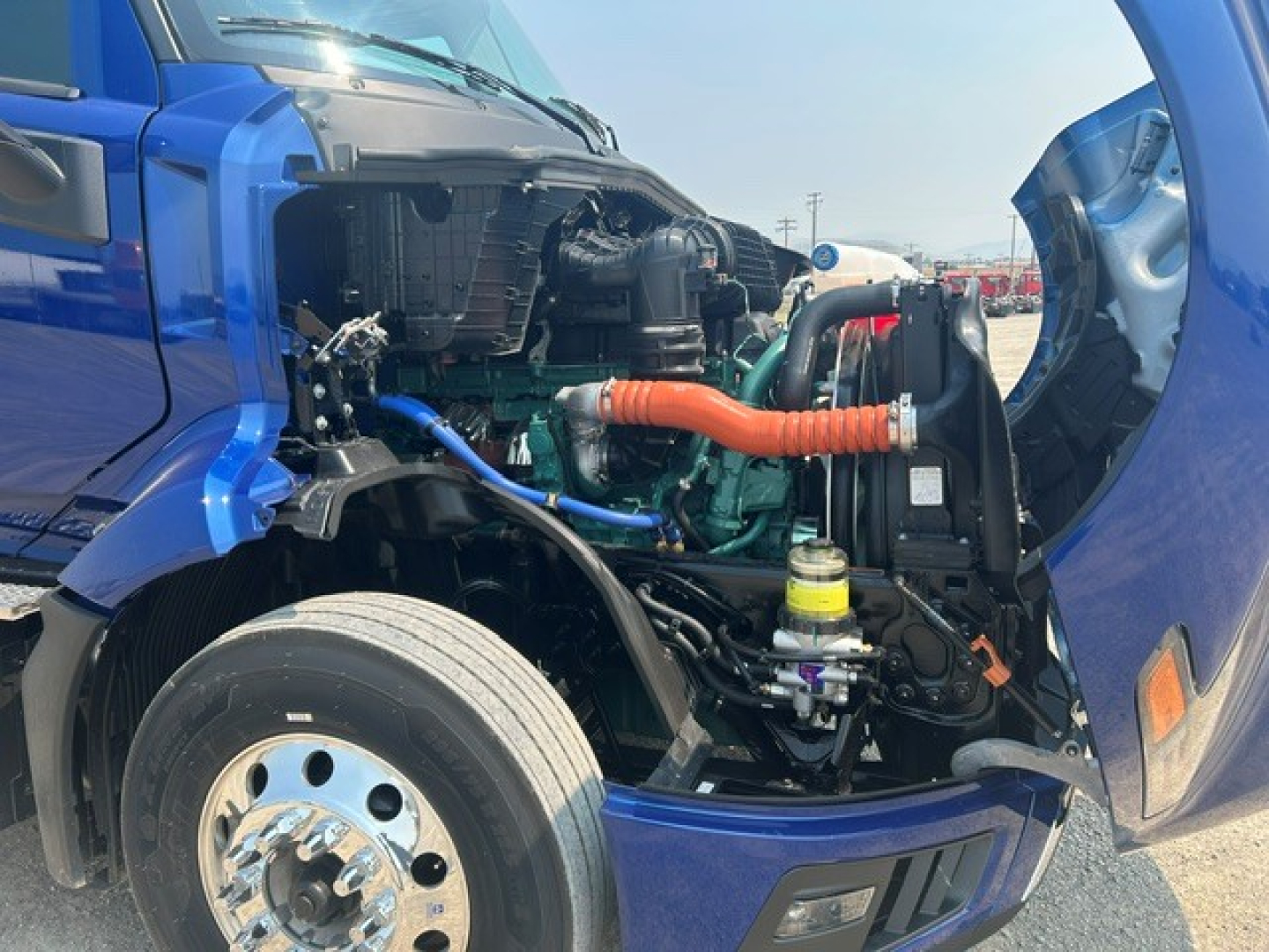 Volvo VNL64T840 engine bay view from the driver side showing orange air intake boot, turquoise hoses, coolant reservoir, and green engine block.