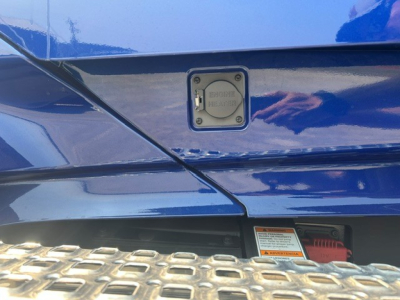 Rear view of a blue Volvo truck showing a fill/maintenance access panel with 'VOLVO' text and a warning label nearby.