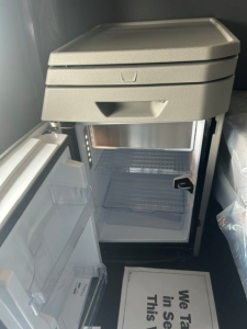 Cabinet area of a truck interior showing a compact refrigerator/freezer unit with open fridge door and empty shelves inside.