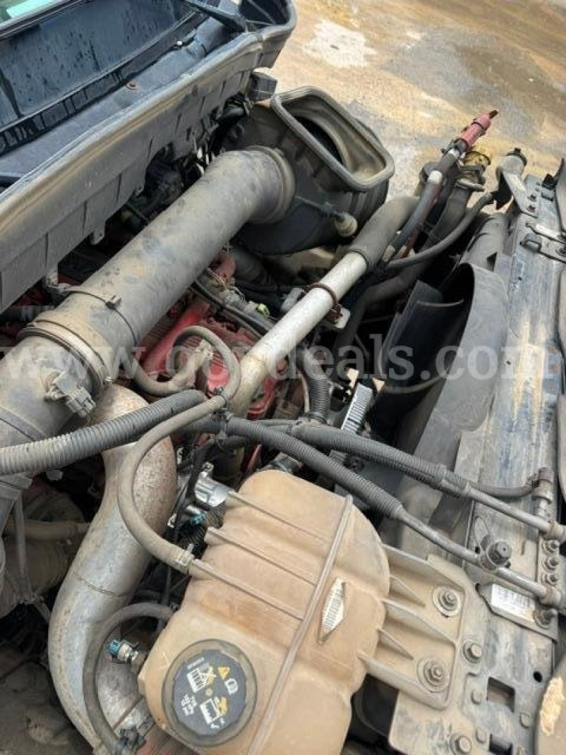 Truck engine bay showing coolant reservoir and various hoses and belts in a 2021 International HV607 engine bay.