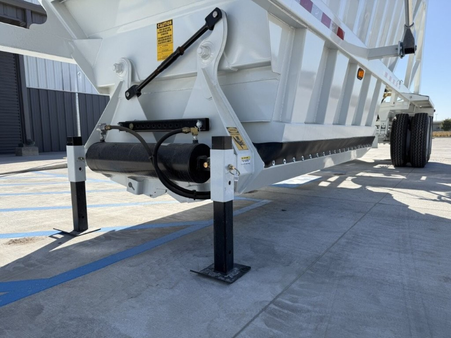 Dump trailer hitch area showing A-frame legs, hydraulic cylinder, and underside of Armor Lite SBD40 skeleton dump trailer.