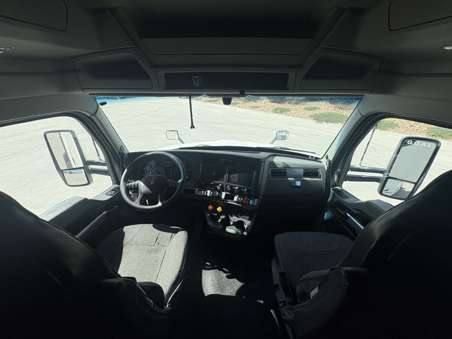 Kenworth T680 cab interior showing steering wheel, dashboard, and front seats; windshield and side mirrors visible.