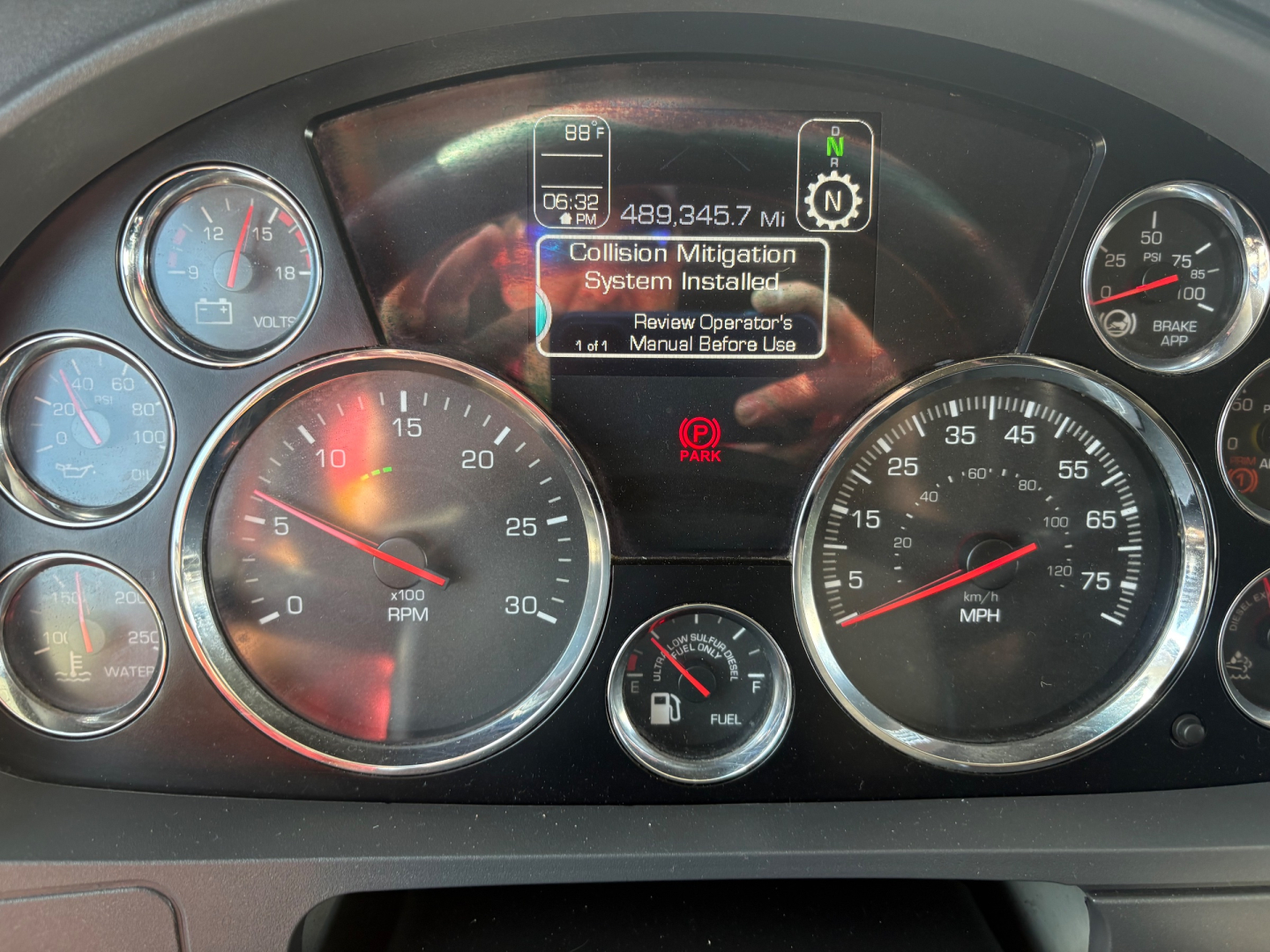 Kenworth-T680 instrument cluster showing digital display and analog gauges; center screen reads 'Collision Mitigation System Installed' with maintenance message; surrounding gauges indicate RPM, MPH, fuel, etc.