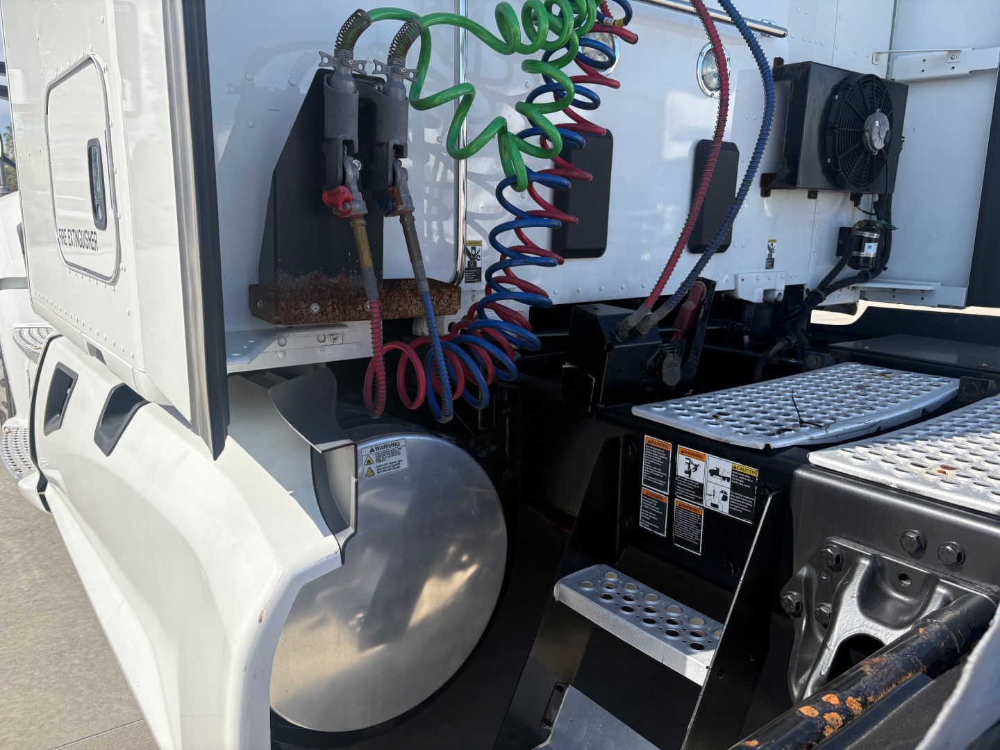 Kenworth T680 truck rear cab area showing air hoses, electrical connectors, and battery/step area.