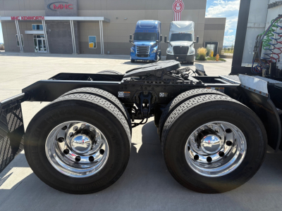 Kenworth T680 chassis rear dual rear wheels showing chrome rims and frame, with cab trucks in background at dealership