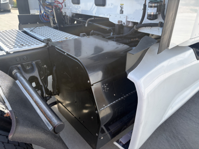 Kenworth T680 engine bay area showing black toolbox/footwell cover and surrounding components; visible cab step area and chassis near the driver side.