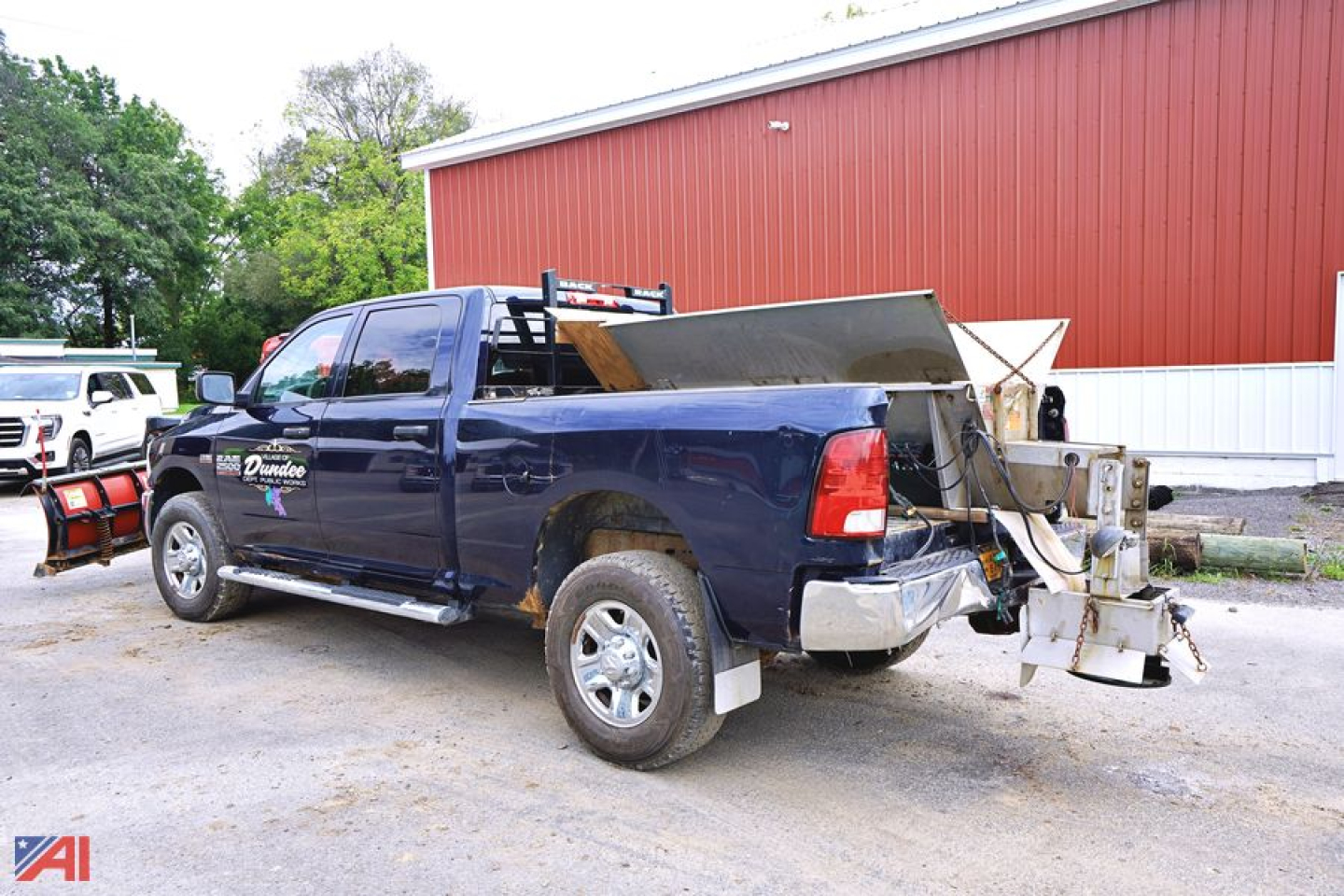 Ram 2500HD crew cab pickup with V-plow and spreader mounted in rear, blue color, side steps, daytime outdoor lot.