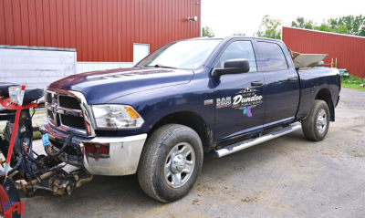 Ram 2500 pickup with V-plow and spreader in service bay showing front-left view and side decal