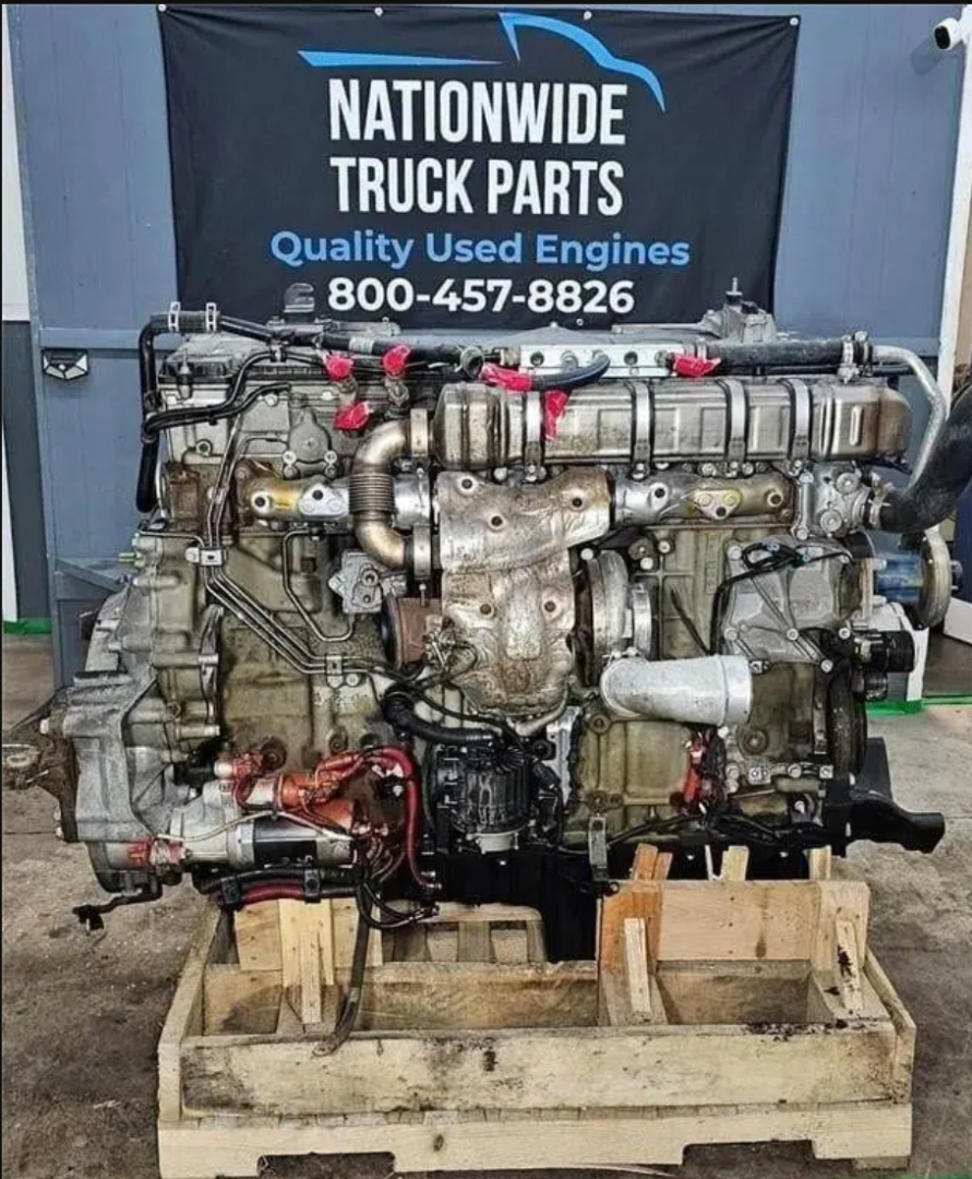 Engine showing Detroit DD15 powerplant mounted on wooden pallet with hoses and components visible, banner reading Nationwide Truck Parts in background.