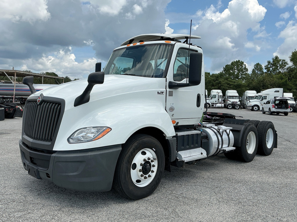 Truck cab and chassis showing International LT625 daycab with white paint and dual rear axles in a dealership lot.