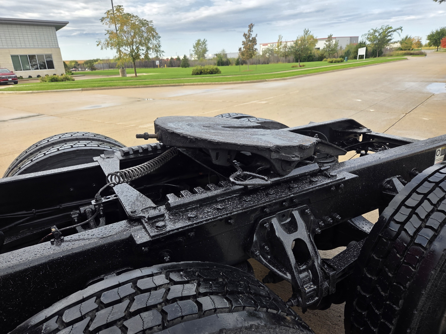 Vehicle chassis of a Kenworth truck showing frame rails, suspension components, and rear wheels; wet surfaces.