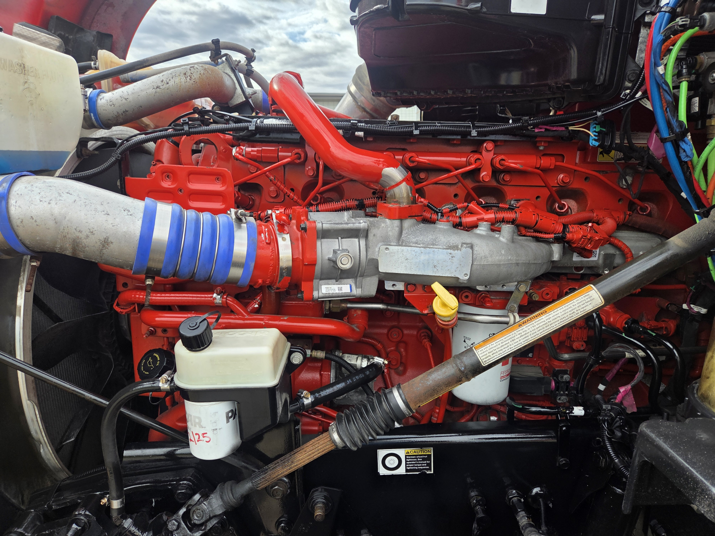 Kenworth T680 engine bay showing bright red engine block and side-mounted turbo, hoses, and wiring harnesses.