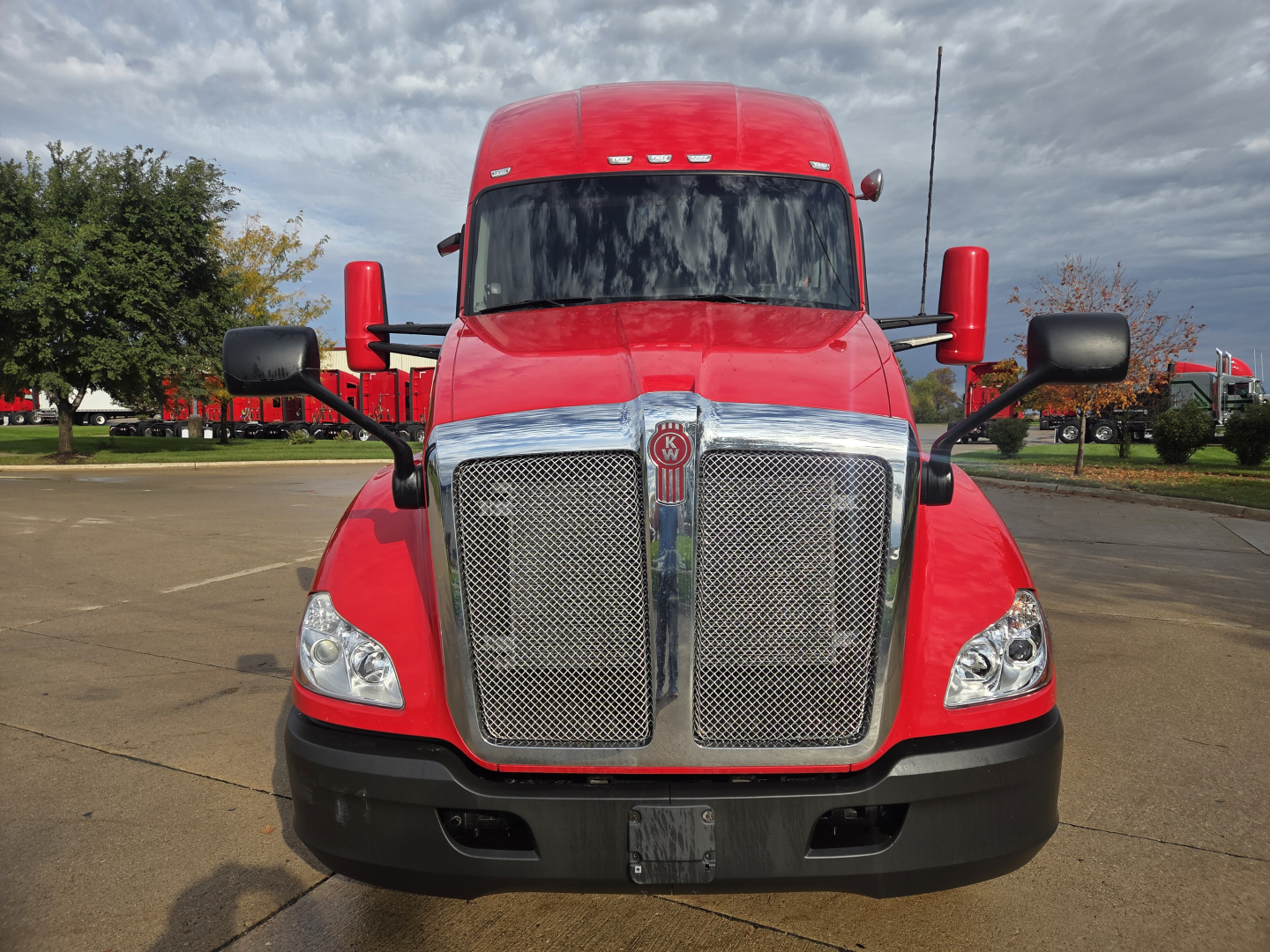 Kenworth T680 front view showing large chrome grille, red cab, black bumper, two side mirrors, and daytime running lights.